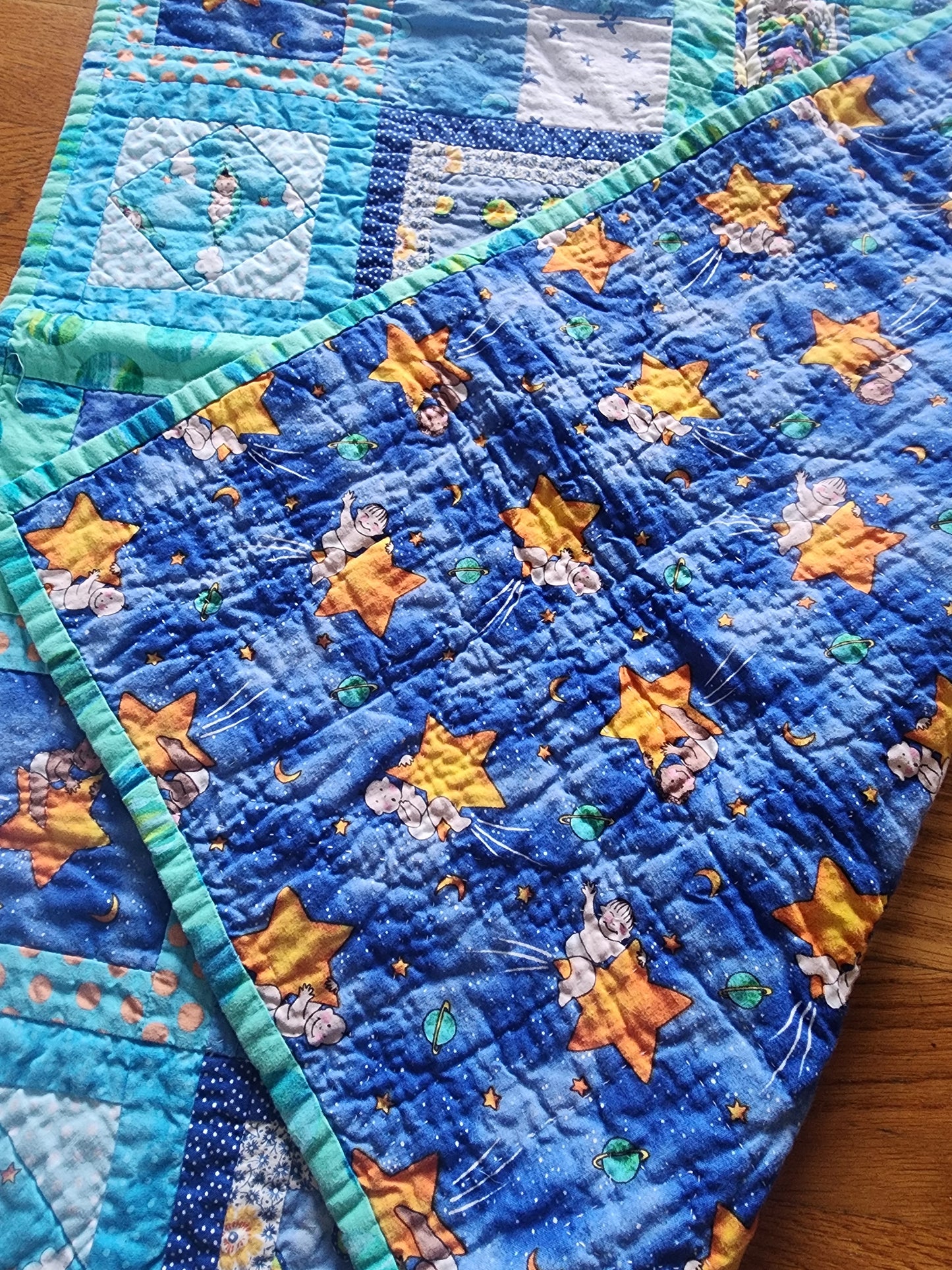 Homemade baby quilt in blues greens and Yellows baby's riding stars.